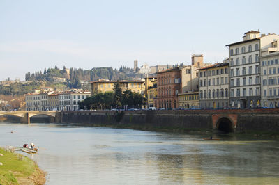 Bridge over river by buildings against clear sky