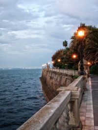 Illuminated street by sea against sky