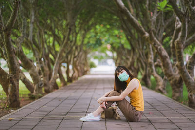 Woman sitting on footpath amidst plants against trees