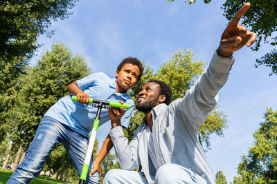 Low angle view of young man riding push scooter against sky