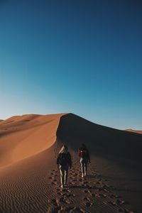 Rear view of friends walking on desert against clear blue sky