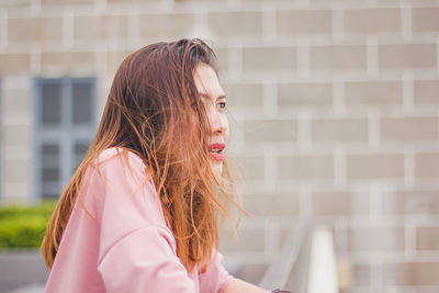 Portrait of young woman looking down against brick wall