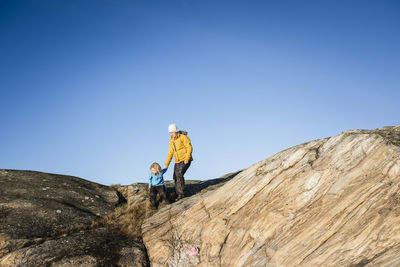 Low angle view of people on mountain against clear blue sky