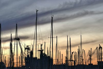 Sailboats moored at harbor against cloudy sky