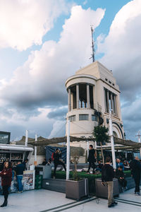 People in front of building against cloudy sky