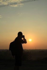 Silhouette man photographing at sunset