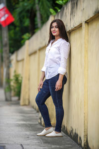 Full length of young woman standing against building