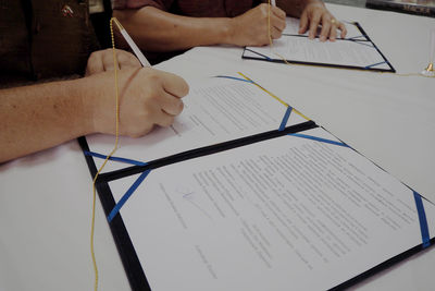 Midsection of people writing in book on table