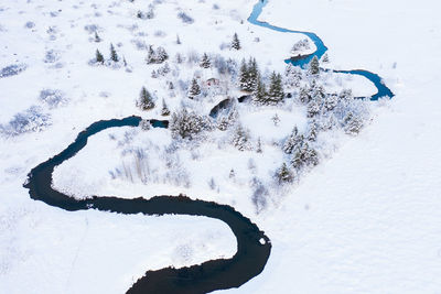 House near river between trees and fields in snow