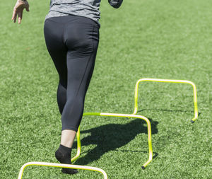 Rear view of woman running over hurdles on turf