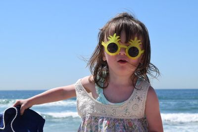 Portrait of beautiful young woman standing at beach against clear sky