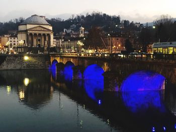 Illuminated bridge over river by buildings in city at night