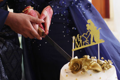 Close-up of bride and bridegroom cutting wedding cake