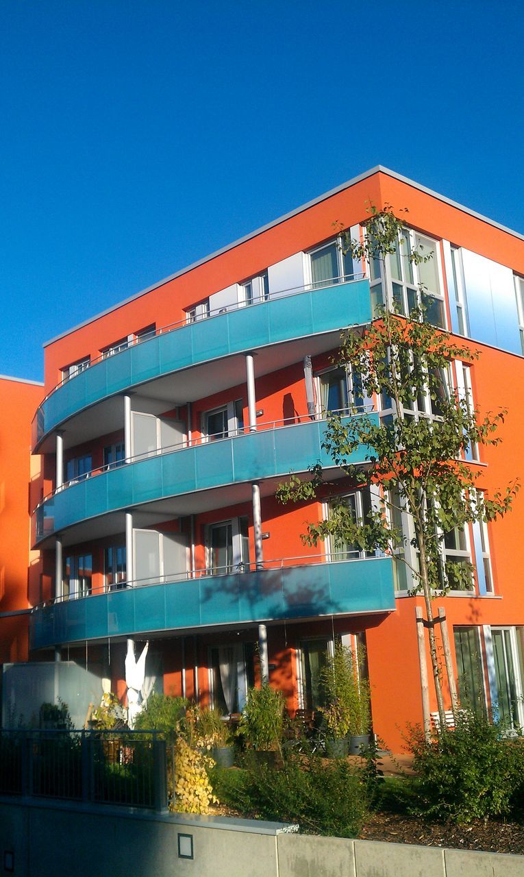 architecture, building exterior, built structure, clear sky, blue, low angle view, residential building, residential structure, building, city, balcony, potted plant, window, sunlight, house, copy space, growth, day, outdoors, tree