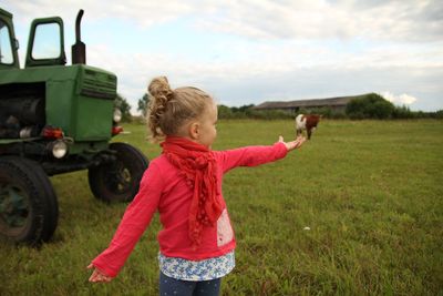Optical illusion of girl holding cow on grassy field by tractor against sky