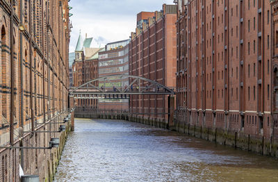 Bridge over canal by buildings against sky