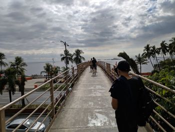 Rear view of people walking on footbridge against sky