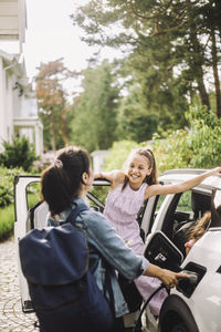 Woman charging electric car while talking to smiling daughter