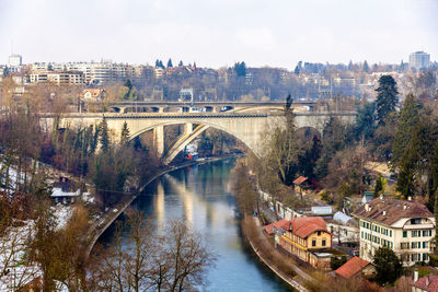 Bridge over river by buildings in city against sky