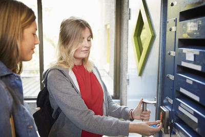 Female student standing by friend while unlocking door with cardkey at university