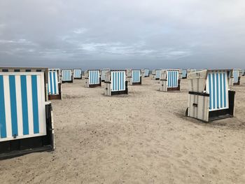 Hooded chairs on beach against sky