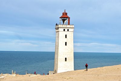 Lighthouse on beach by sea against sky