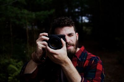 Portrait of young man photographing camera in forest