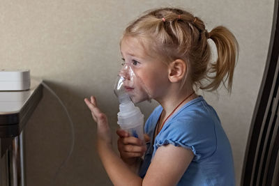 Little girl makes inhalation with a nebulizer at home, sitting on a chair. 