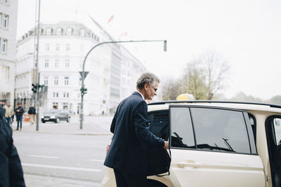 Mature businessman by taxi door in city