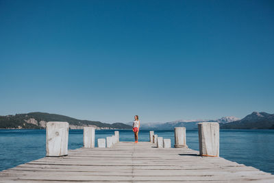 Rear view of woman standing on pier at sea against clear blue sky