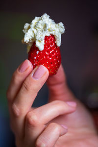 Close-up of hand holding strawberry with whipped cream