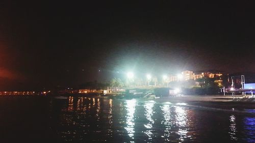 Illuminated buildings by river against sky at night