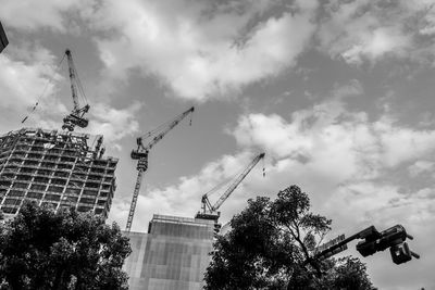 Low angle view of crane by building against sky