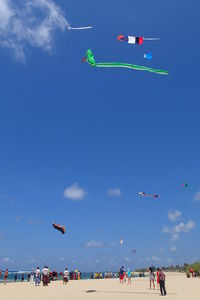 People with flag at beach against blue sky
