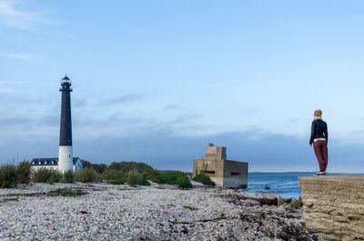 Lighthouse by sea and buildings against sky