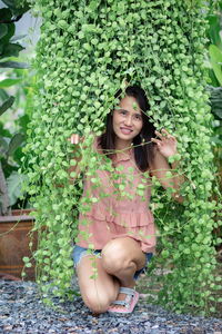 Portrait of smiling woman crouching by plants