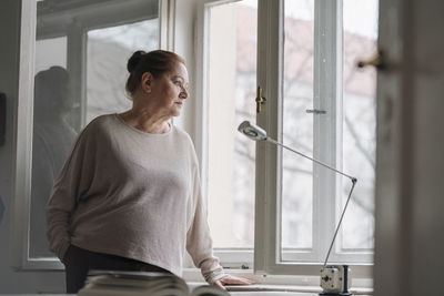 Serious senior woman looking out of window at home