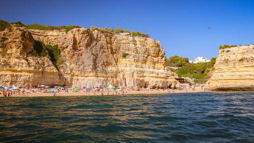 People on rocks by sea against clear sky