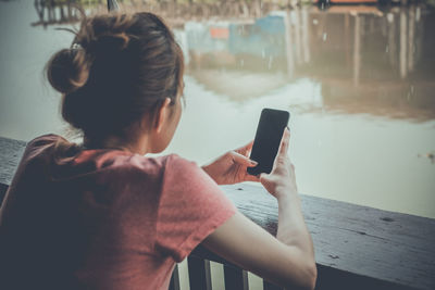 Rear view of woman using mobile phone against lake