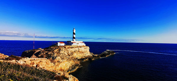 Lighthouse by sea against blue sky