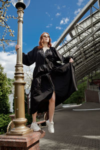 Full length of woman in oversized black dress walking to nowhere against built structure outdoors