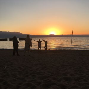 Silhouette people standing on beach against sky during sunset