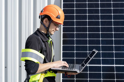 Young engineer working on laptop by solar panel at solar power station