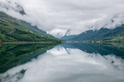 Scenic view of river with clouds reflections amidst green mountains