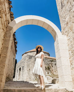 Low angle full length image of young woman wearing white dress standing in stone street in old town.