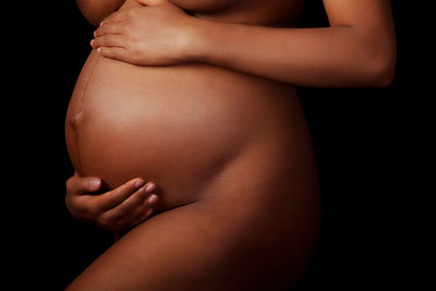 Midsection of woman touching hair over black background