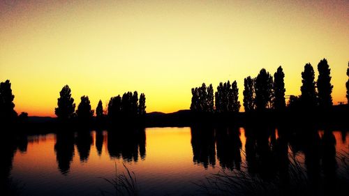 Silhouette trees by lake against orange sky