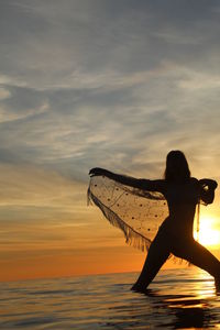 Silhouette woman on beach against sky during sunset