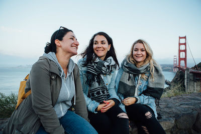 Smiling female friends sitting by golden gate bridge