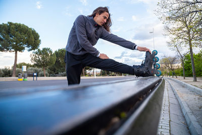 Young man wearing roller skates stretching on bench